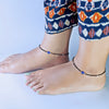 Two feet wearing anklets with a blue eye charm on a light background
