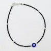 Anklet with black beads and a blue evil eye charm on a light gray background