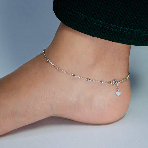 Silver anklet on a person's ankle against a neutral background
