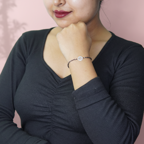 Woman wearing a black beaded bracelet with a silver flower charm against a soft pink background.