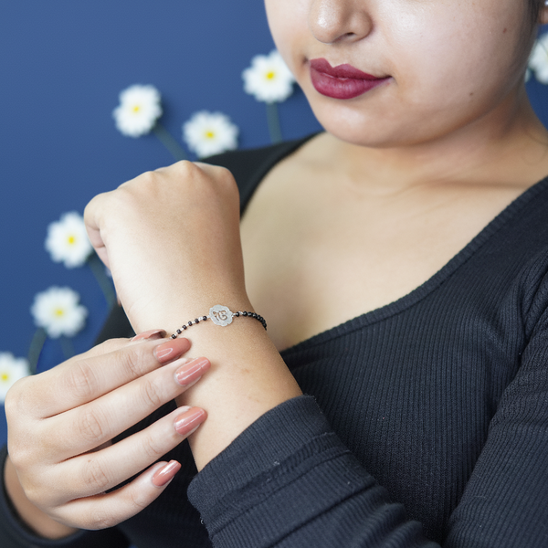 Black beaded bracelet with a silver flower charm worn by a woman against a blue background with white floral accents.