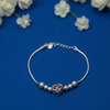 Silver beaded infinity heart bracelet with a rose-gold heart charm displayed on a blue surface decorated with white flowers.