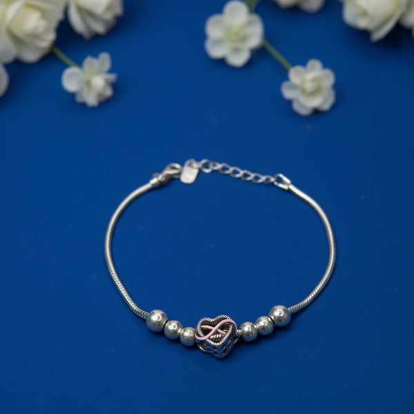 Silver beaded infinity heart bracelet with a rose-gold heart charm displayed on a blue surface decorated with white flowers.