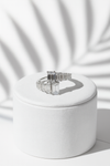Silver ring with emerald-cut gemstones on a white cushion against a white background