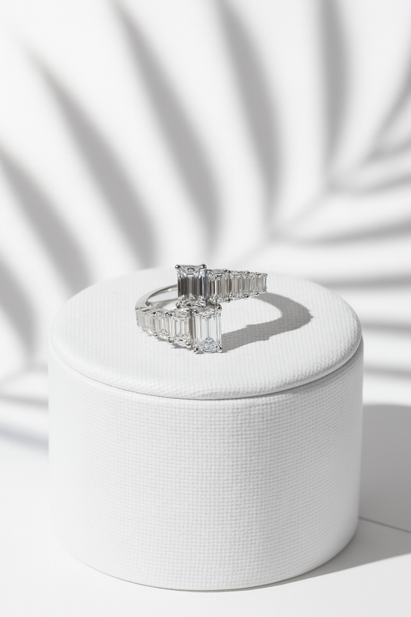 Silver ring with emerald-cut gemstones on a white cushion against a white background