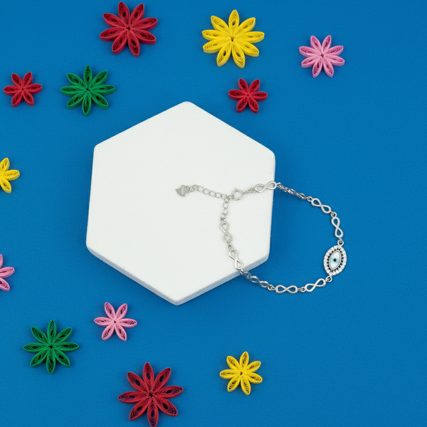 Silver infinity-link Evil Eye bracelet with a blue Nazar charm displayed on a blue background surrounded by colorful decorative flowers.