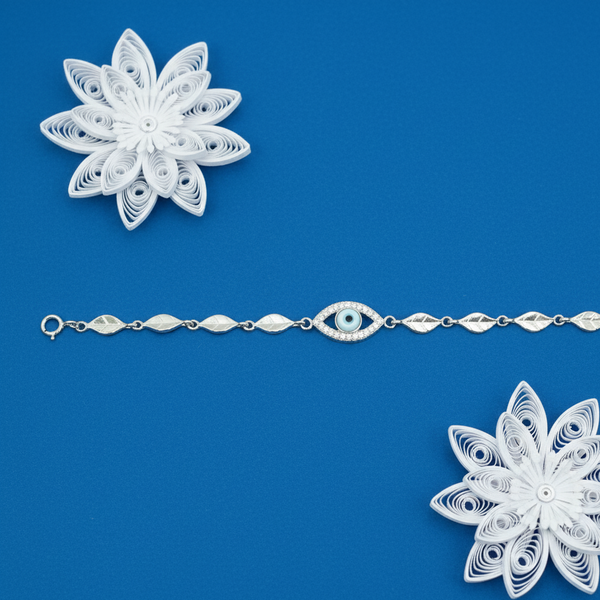 Silver Evil Eye bracelet with leaf links displayed on a blue background with white floral decorations.