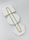 Two-tone gold and silver necklace on a white geometric display stand against a light gray background