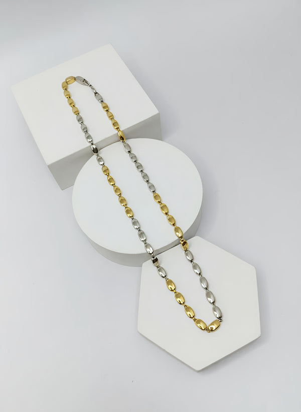 Two-tone gold and silver necklace on a white geometric display stand against a light gray background
