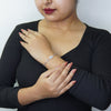 Woman wearing a silver infinity-link bracelet with a blue Evil Eye charm while posing in a black top.