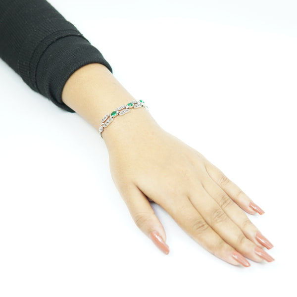 Close-up of a vintage silver bracelet with emerald-green stones worn on a woman's wrist.