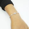 Close-up of a silver Evil Eye bracelet with leaf links worn on a woman's wrist.