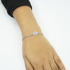 Close-up of a silver infinity Evil Eye bracelet with a blue Nazar charm worn on a woman's wrist against a white background.