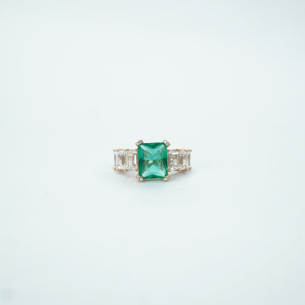 Emerald ring with diamond accents on a light gray background