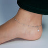 Silver anklet on a person's ankle against a neutral background