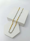 Two tone gold and silver chain necklaces on a white geometric stand.