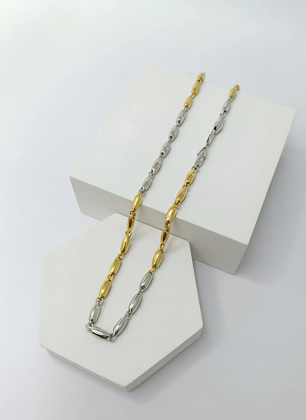 Two tone gold and silver chain necklaces on a white geometric stand.