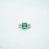 Emerald ring with diamond accents on a light gray background