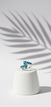 Blue ring on a white pedestal with a palm leaf shadow on a light gray background