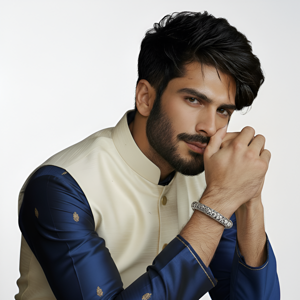 Man wearing a traditional outfit with a white and blue design on a plain background highlightinng silver kada